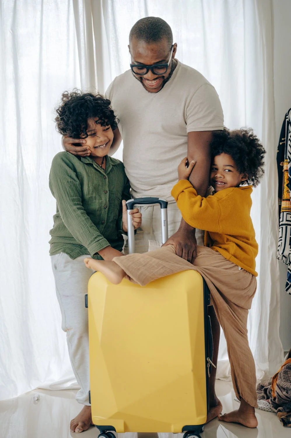 A man walks alongside two children, all of them holding onto a bright yellow suitcase as they travel together. The children appear cheerful, and the man is gently guiding them. The vibrant suitcase stands out, adding a sense of excitement and adventure to the scene.